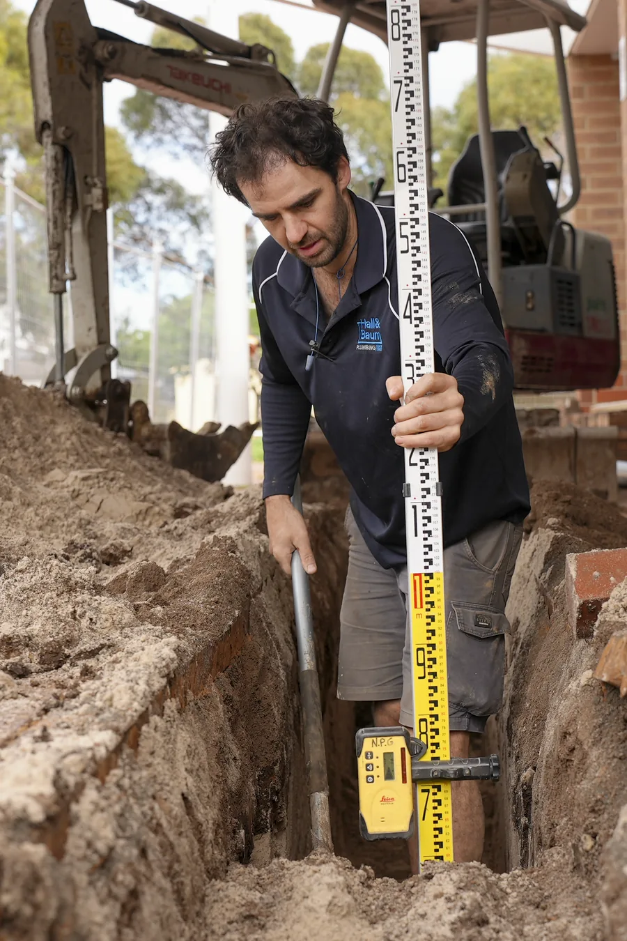 Hall & Baum plumber checking levels in an excavated trench